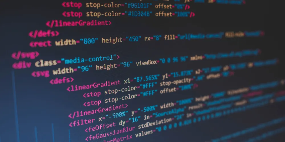 Close-up angled shot of SVG source code on a monitor with pink and blue syntax highlighting against a dark background